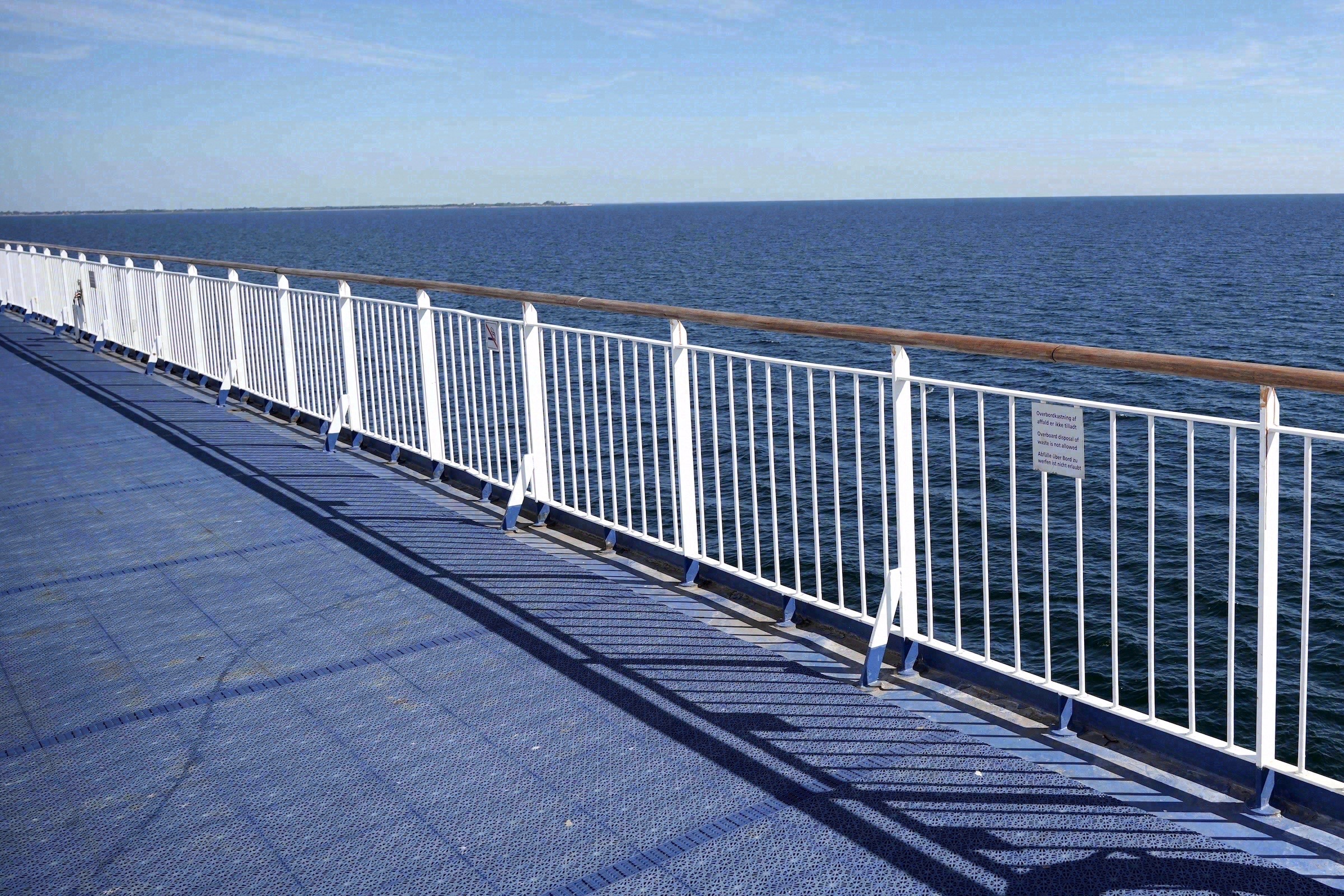View across the outer deck of a ferry with a white railing looking out to the open sea